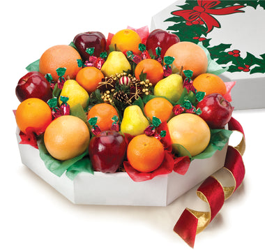 A festive fruit wreath gift box with an assortment of Navel Oranges, Ruby Red Grapefruit, Mandarin Oranges, Apples, Pears, and strawberry-filled hard candies, decorated with a red ribbon and holly design.