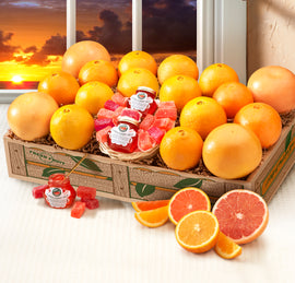 A gift basket containing an assortment of citrus fruits including red grapefruits, orange navels, and scarlet navels, alongside jars of marmalade and citrus candies, presented in front of a sunset backdrop.